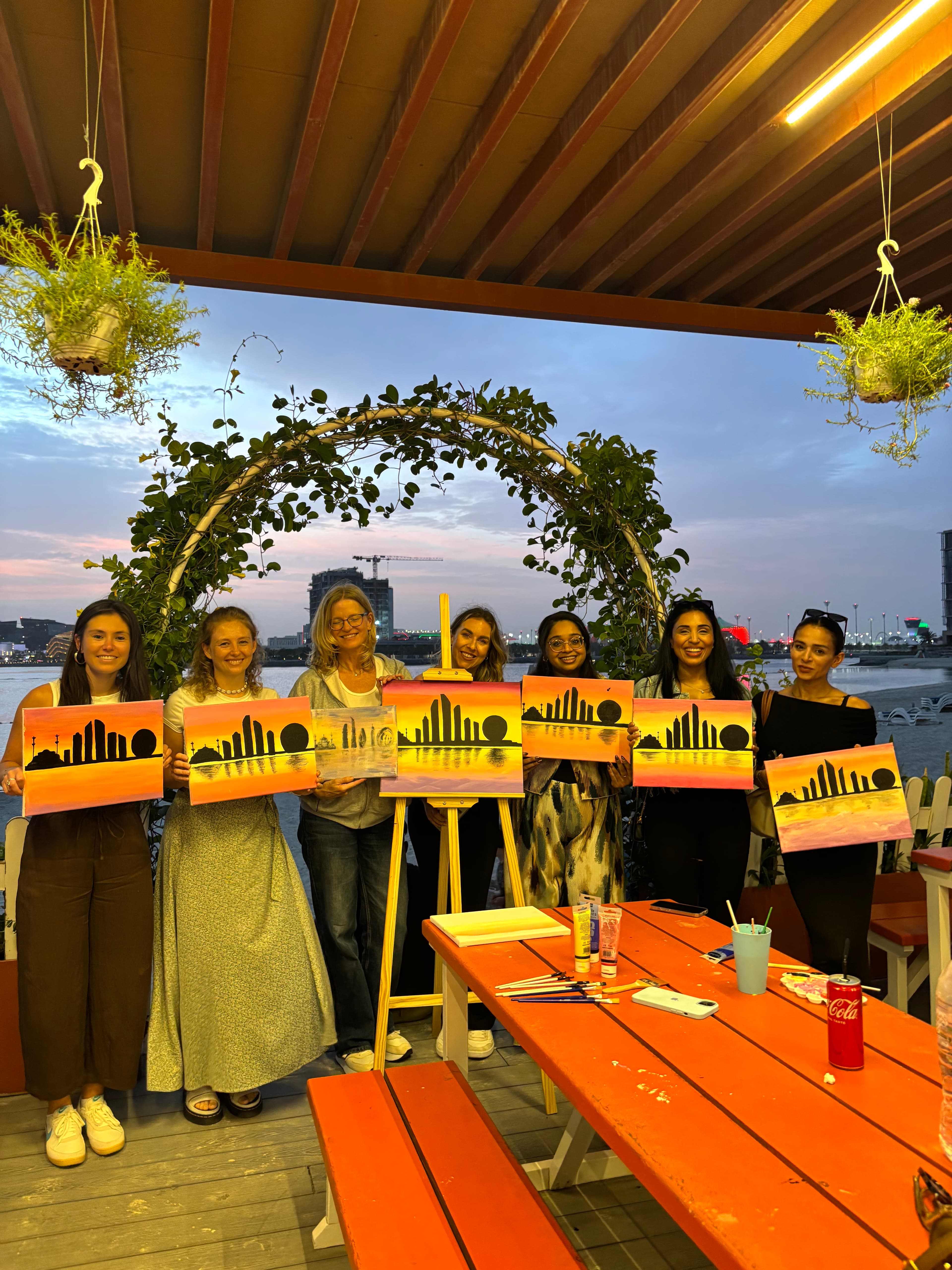 Group holding city skyline paintings at sunset outdoors